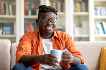Cheerful african american guy wearing eyeglasses drinking tea at home