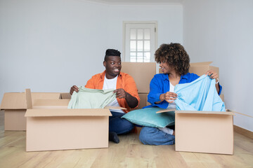 Happy Black Spouses Unpacking Boxes With Clothes After Moving To New Home