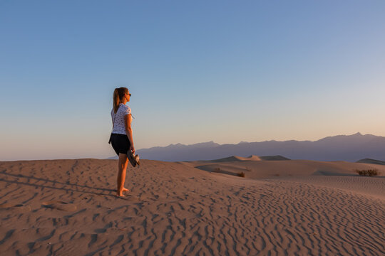 Touristic woman enjoying the sunrise with scenic view on Mesquite Flat Sand Dunes, Death Valley National Park, California, USA. Morning walk in Mojave desert with Amargosa Mountain Range in back.