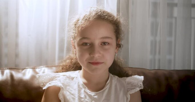 Portrait Funny little girl smiling child looking at camera are sitting on the couch at home, cute kid child with pretty face sitting on sofa. Concept of a happy childhood. 4K