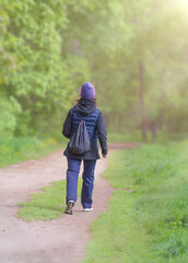 A woman from behind walks along a forest path with backpacks on a sunny spring day in nature. Outdoor hiking, healthy lifestyle.