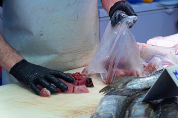 Gloved fishmonger's hands placing pieces of tuna in a plastic bag to be weighed and sold to the customer.