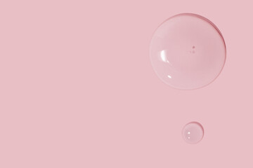 large drops of cosmetic serum, liquid, water, gel on a pink background