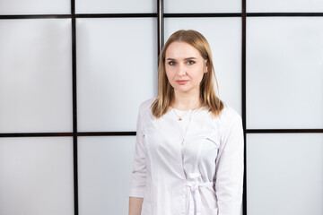 Portrait of a young blonde doctor in a white uniform on a black and white background.
