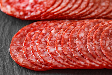 Salami sausage meat with bacon cut into circles in two rows close-up on slate stone plate, dark background, side view, selective focus.