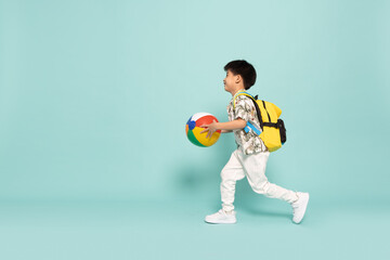 Asian little boy in flower pattern summer outfits holding beach ball and running with backpack isolated on green background, Five years old