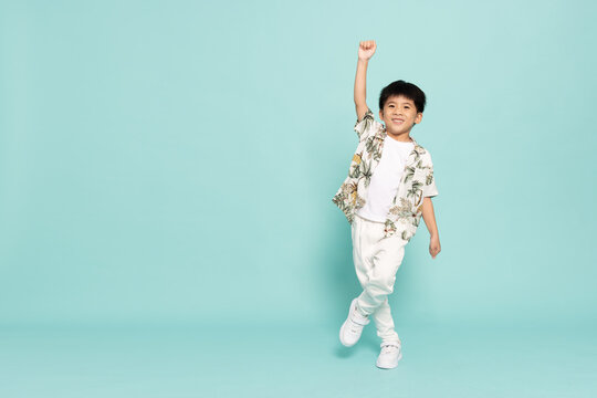 Asian little boy in summer outfits standing and raise hand isolated on green background