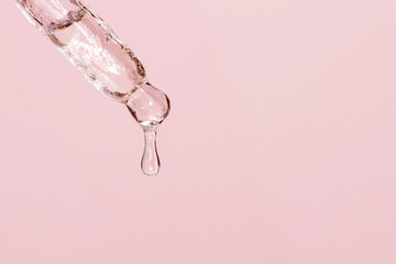 Cosmetic pipette with dripping liquid and drops on a pink background, serum, serum, gel, vitamin,...