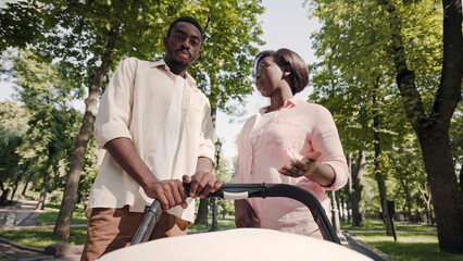 Happy black parents walking with baby stroller, discussing who the baby looks alike