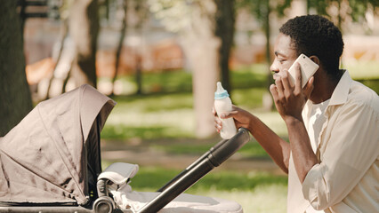 Irritated father talking on phone, trying to feed newborn in park, parenthood