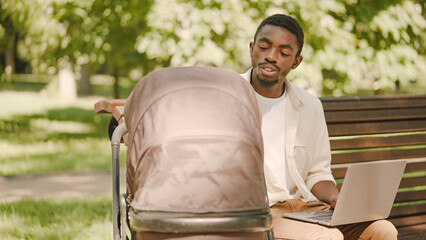 Businessman father working on laptop and taking care of child in baby stroller