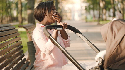 Young mother yawning, rocking baby in the stroller, exhaustion of motherhood - obrazy, fototapety, plakaty