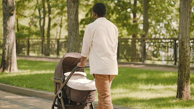 Young man walking with baby stroller in park, paternal leave, family