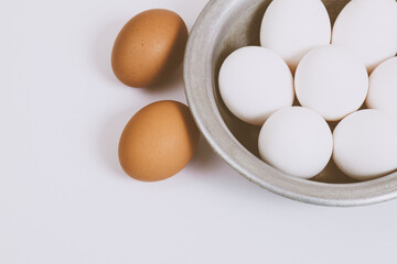 Brown eggs on bright background and white eggs in metal bowl. Close up, selective focus. Concept scene. 