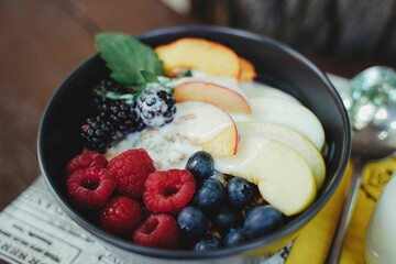 Closeup of different fresh fruits and various berries in a black bowl with a glass of milk