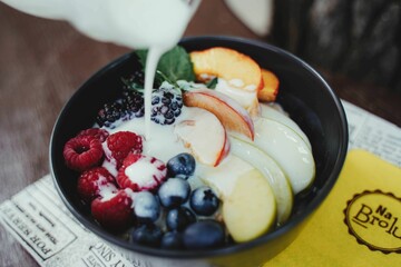 Closeup of different fresh fruits and various berries in a black bowl with a glass of milk