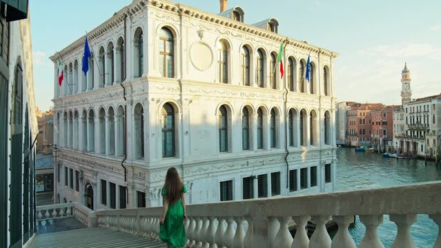 Female tourist exploring the Rialto Bridge in 4K. A young woman runs down the bridge towards a building with Italian flags by the Grand Canal in the heart of Venice, Italy.