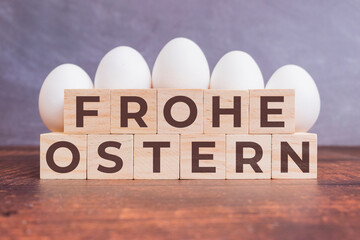 Frohe Ostern auf Holzwürfeln vor weißen Eiern stehend und liegend auf einem Holztisch