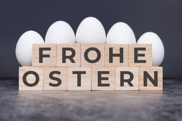 Frohe Ostern auf Holzwürfeln vor weißen Eiern, die auf einem steinernen Untergrund stehen.