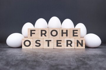 Frohe Ostern auf Holzwürfeln vor weißen Eiern stehend und liegend auf einem Steinuntergrund....