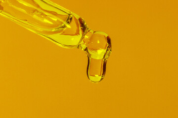 Cosmetic pipette with dripping liquid, oil and drops on a yellow background, serum, serum, gel, vitamin, water, oil
