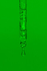 Cosmetic pipette with dripping liquid, oil and drops on a green background, serum, serum, gel, vitamin, water, oil. Natural cosmetic