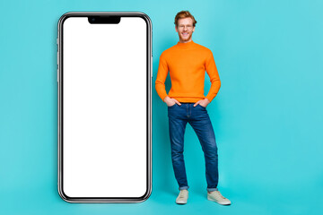 Photo of pretty cool young man wear orange pullover spectacles modern device empty space isolated teal color background