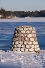 A man-made pile of rocks against a frozen lake on a sunny winter day.