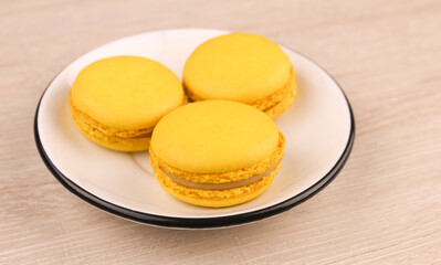 Three yellow macaroons in a white saucer on a wooden background