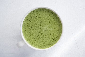 Green tea in a white mug on a white background, photo from above. Matcha foamed, dietary and healthy drink.