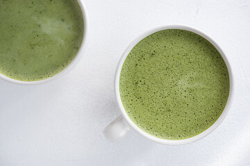 Green tea in a white mug on a white background, photo from above. Matcha foamed, dietary and healthy drink.