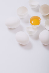 Whole white chicken eggs and cracked egg half with a yolk inside on bright background. Selective focus.
