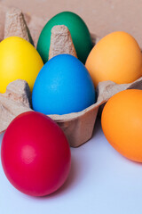 Painted eggs in egg tray on light background. Colorful Easter eggs. Macro shot, selective focus. 