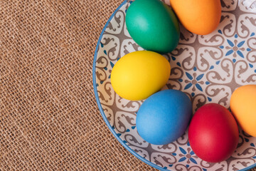 Painted eggs. Colorful Easter eggs in the plate on sackcloth. Macro shot, selective focus. Top view.