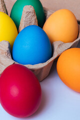Painted eggs in egg tray on light background. Colorful Easter eggs. Macro shot, selective focus. 