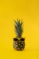 Fresh pineapple with sunglasses on yellow background. Minimal summer furit concept.
