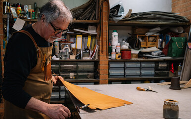 side view of a leather craftsman who dabs the edges of a piece of leather with a waterproof varnish