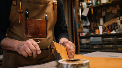 selective focus on the hands of a leather craftsman who dabs the edges of a piece of leather with a waterproof varnish
