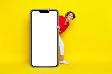 Full body portrait of charming positive lady peeking behind empty space billboard isolated on yellow color background - obrazy, fototapety, plakaty