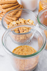 Ingredients for cheesecake. Stack of cookies, caramel, peanuts, grinded cookies, cream in glassware on table. Selective focus.