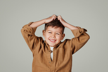 Cheerful excited little european boy holding hands on his head, has fun, enjoy spare time