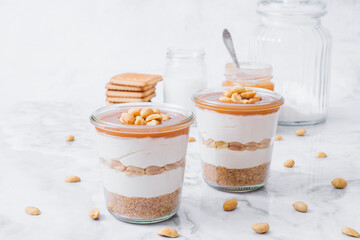 Cheesecake in a jar. Layers of grinded cookies, caramel, peanuts and  cream cheese. Covered in caramel and decorated with peanuts. Selective focus. Macro shot.