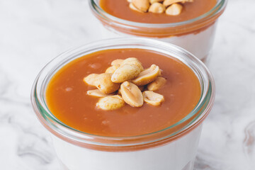 Cheesecake in a jar. Layers of grinded cookies, caramel, peanuts and  cream cheese. Covered in caramel and decorated with peanuts. Close-up photo. Selective focus. Macro shot.