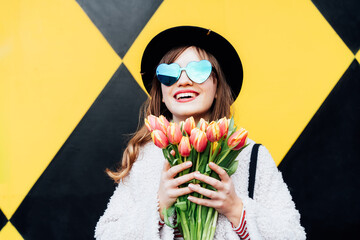 Happy. emotional young fashion woman in heart-shaped sunglasses holding bouquet of fresh tulip...