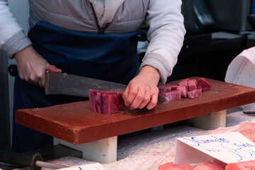 Woman fishmonger cutting pieces of tuna with a large knife on a board at a fish market.