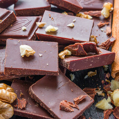 broken chocolate with nuts and cinnamon on black background