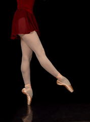 slender legs of a ballerina in ballet shoes, on a black background, copy space.

