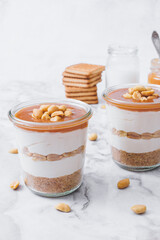 Cheesecake in a jar. Layers of grinded cookies, caramel, peanuts and  cream cheese. Covered in caramel and decorated with peanuts. Selective focus. Macro shot.