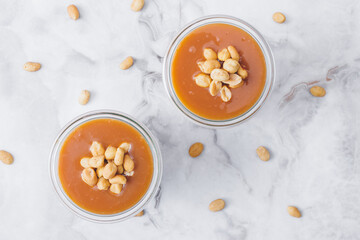 Glass jars with caramel, decorated with salty peanuts on table. Top view.