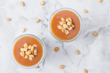 Glass jars with caramel, decorated with salty peanuts on table. Top view.